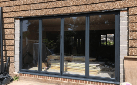 Renovation materials stacked inside a building visible through large glass windows with reflective surface and stone exterior.