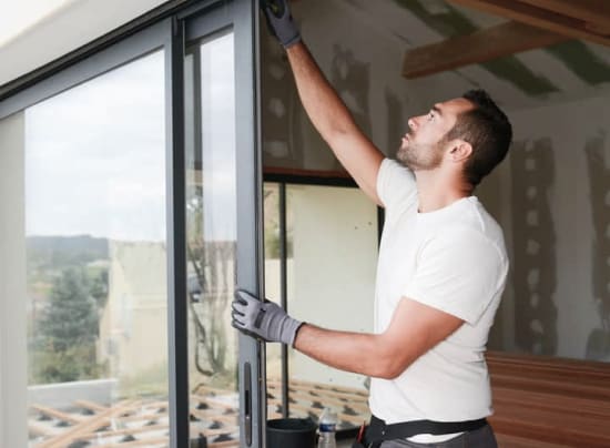 A man in a white shirt and gloves installing a sliding glass door in a modern home.