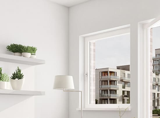 View from a bright room looking out of an open window showing a modern apartment building. shelves with plants and a lamp are visible inside.